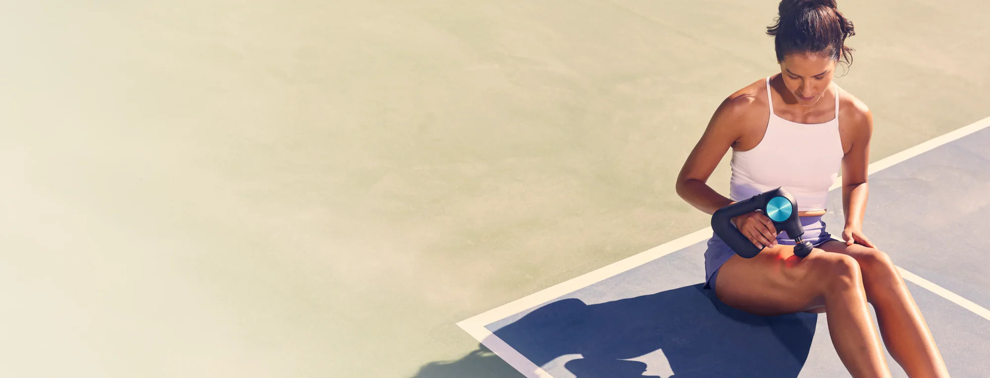 Woman sitting on a blue mat on a tennis court, holding a water bottle.